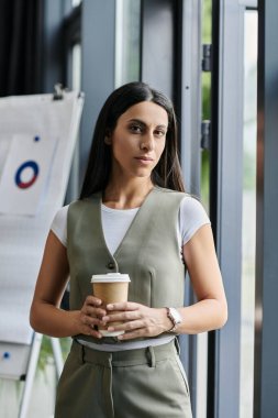 Genç bir kadın bir ofiste elinde kahve fincanıyla kameraya bakıyor..