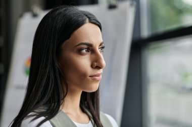 Uzun siyah saçlı genç bir kadın bir girişim üzerinde çalışırken pencereden dışarı bakar..