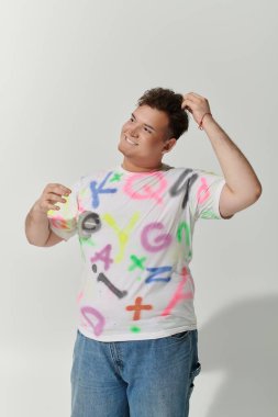 İbne biri parlak bir şekilde gülümser, beyaz bir tişört giyer ve renkli grafitiler çizer..