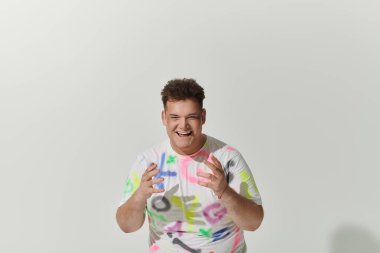 Eşcinsel bir insan parlak bir şekilde gülümser, beyaz bir tişört giyer ve soyut tasarımlar yapar..