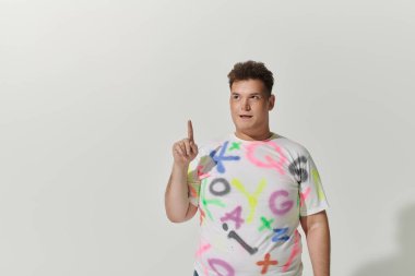 Beyaz tişörtlü, renkli grafitileri olan tuhaf bir adam parmağıyla işaret ediyor..