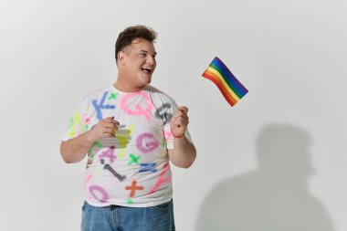 Renkli gömlekli bir adam gökkuşağı bayrağı sallarken gülümsüyor..