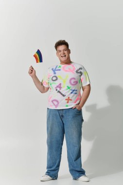 A queer person with a rainbow flag smiles brightly, standing against a white background. clipart