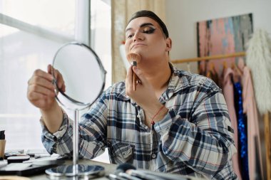 Ekose gömlekli bir eşcinsel aynaya bakarken makyaj yapar..