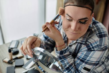 Eşcinsel bir insan aynaya bakarken makyaj yapar..