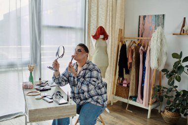 Eşcinsel biri aynanın önüne makyaj yapar. Etrafı şık kıyafetlerle çevrilidir..