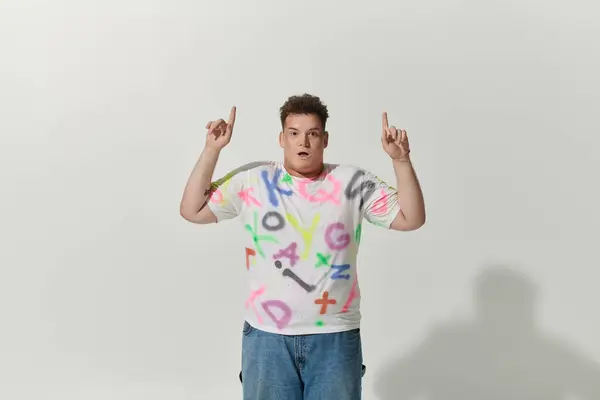 stock image A queer person in a brightly colored shirt points upwards with both hands.