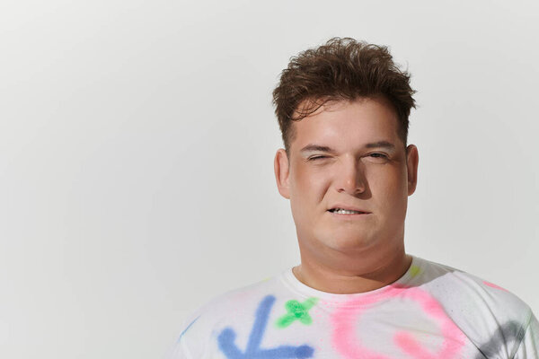 A young queer person, wearing stylish clothing with colorful accents, stares directly at the camera.