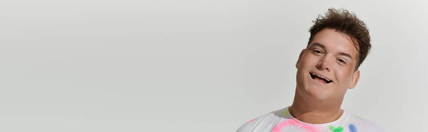 A queer person in fashionable attire smiles playfully against a white backdrop.