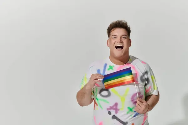 stock image A smiling man with colorful clothing holds a rainbow pride flag.