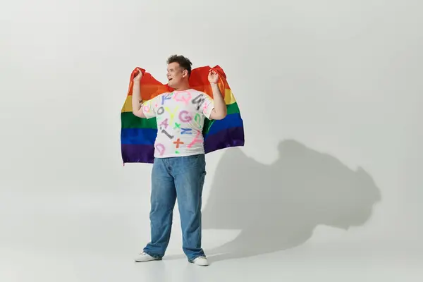 stock image A queer person draped in a rainbow flag smiles confidently.