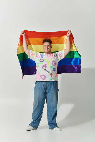 A smiling queer person holds a rainbow flag high, celebrating pride and individuality.