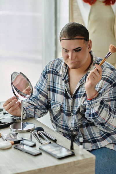 странный человек в клетчатой рубашке наносит макияж, окруженный кисточками и палитрами