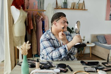 Eşcinsel bir insan, çeşitli güzellik ürünleriyle çevrili bir aynanın önünde makyaj yapar..