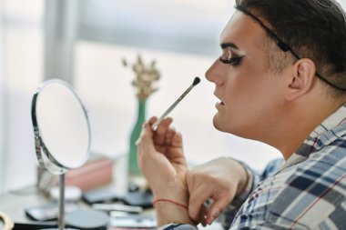 Eşcinsel bir insan aynanın önünde makyaj yapar..