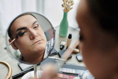 Eşcinsel bir insan aynaya bakarken makyaj yapar, göz makyajına odaklanır..