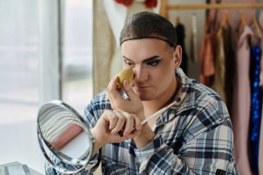 Eşcinsel bir insan aynanın önüne makyaj yapar, göz makyajına odaklanır..