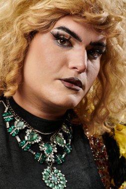 Özenle hazırlanmış makyajı ve büyük yeşil mücevher kolyesi olan tuhaf bir insanın yakın plan portresi..
