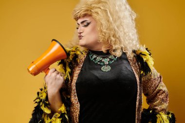 Cesur makyajlı sarışın travesti sağa bakan bir megafon tutuyor.