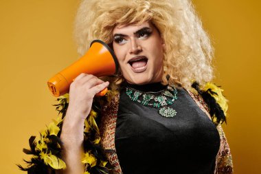Sarışın peruklu ve makyajlı bir travesti kulağına bir megafon tutar..