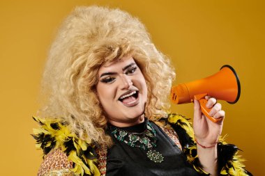 Büyük sarı peruklu bir travesti elinde megafonla gülümsüyor..