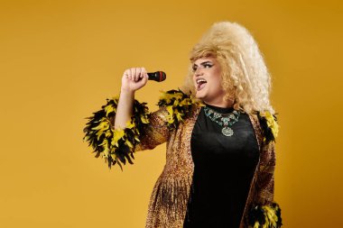 Drag queen sarı peruklu, leopar desenli ceketli şarkı söyler.