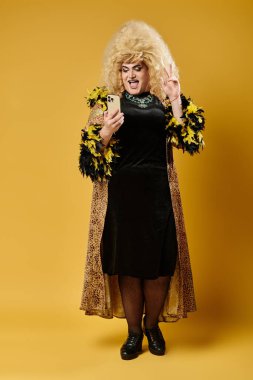Leopar desenli ceketli ve siyah elbiseli bir travesti sarı arka planda bir selfie için poz veriyor..