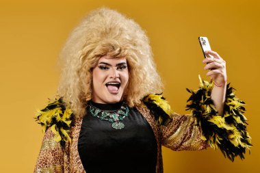 Şık giyinmiş bir travesti neşeli bir ifadeyle selfie için poz verir..