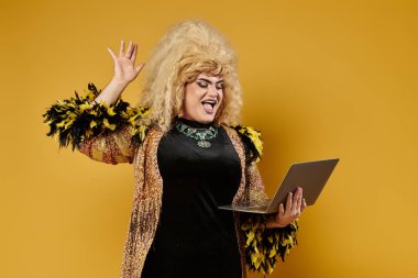 A drag queen in a stylish outfit waves to the camera while holding a laptop. clipart