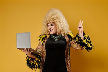 Şık giyinmiş bir travesti dizüstü bilgisayar tutuyor ve barış işareti gösteriyor..