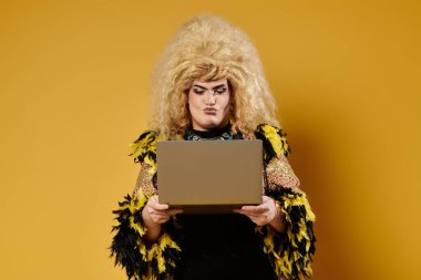 A drag queen in a stylish, feathered outfit uses a laptop against a yellow background. clipart