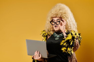 Şık giyinmiş bir travesti ve sarışın bir peruk dizüstü bilgisayara şaşkın şaşkın bakıyor..