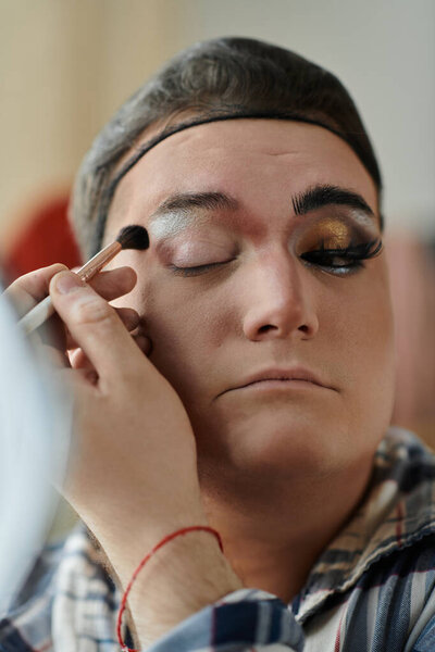 A queer person is getting their makeup done, focusing on their eye.
