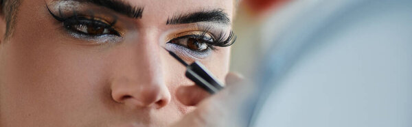 A queer person has their eye makeup applied with a black eyeliner.