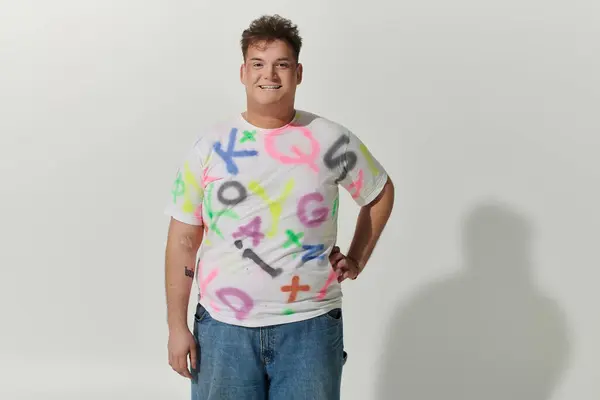 stock image Short, dark-haired queer person in white tee and blue jeans by white wall