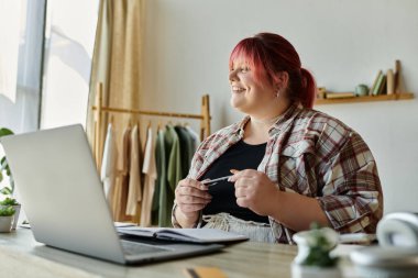 A plus-size woman smiles while working at her home office desk. clipart