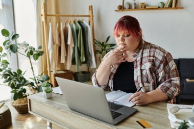 Büyük beden bir kadın evindeki bir masada oturuyor ve bir deftere yazıyor..