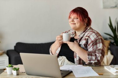 A woman enjoys a cup of coffee while working at her home office. clipart