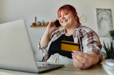 Telefonuyla konuşan ve elinde kredi kartıyla gülümseyen bir kadın..