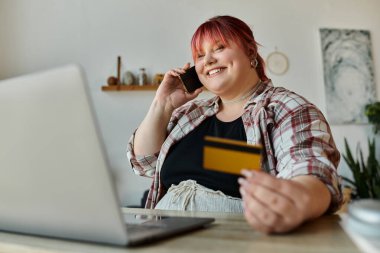 A woman smiles while talking on her phone and holding a credit card. clipart