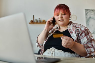 Bir kadın ev ofisinde otururken telefonunu ve kredi kartını satın almak için kullanıyor..