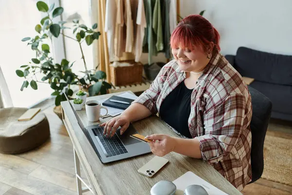 stock image A woman smiles as she makes a purchase online, using a credit card and laptop.