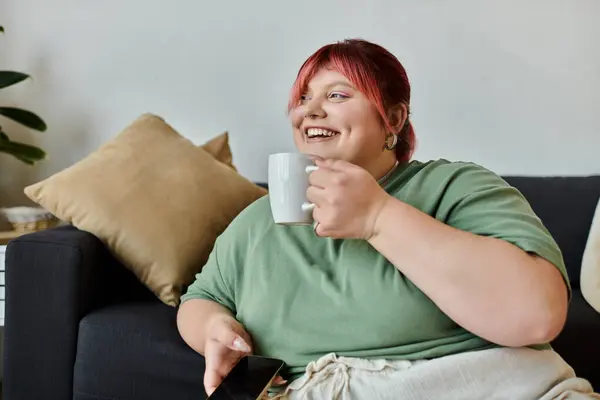 stock image A woman relaxes on a couch, enjoying a warm beverage and the comfort of home.