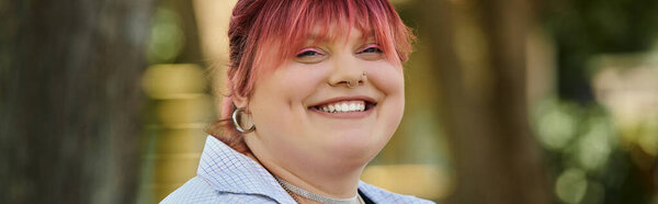 Улыбающаяся женщина с розовыми волосами расслабляется на открытом воздухе.