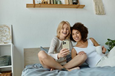 İki kadın, rahat pijamalarını giyip, bir yatakta selfie çekiyorlar..