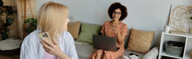 İki kadın, biri dizüstü bilgisayarda, biri akıllı telefonda, kanepede rahatla, evde çalış..