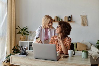 İki kadın evden çalışıyor, biri telefona bakıyor, diğeri de dizüstü bilgisayara..