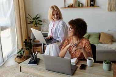 A lesbian couple works from home on their laptops, with one standing and the other sitting. clipart