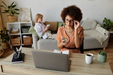 Ortağı kanepede dinlenirken bir kadın oturma odasındaki masada dizüstü bilgisayarıyla çalışıyor..