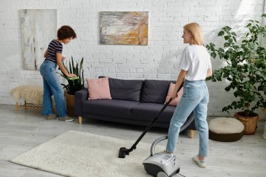 Çok kültürlü lezbiyen bir çift modern dairelerini birlikte temizliyor. Biri etrafı temizliyor, diğeri etrafı süpürüyor..
